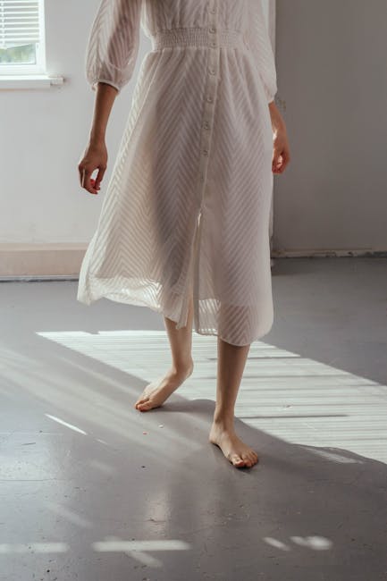 Elegant shot of a barefoot woman in a sheer white dress dancing in soft sunlight.