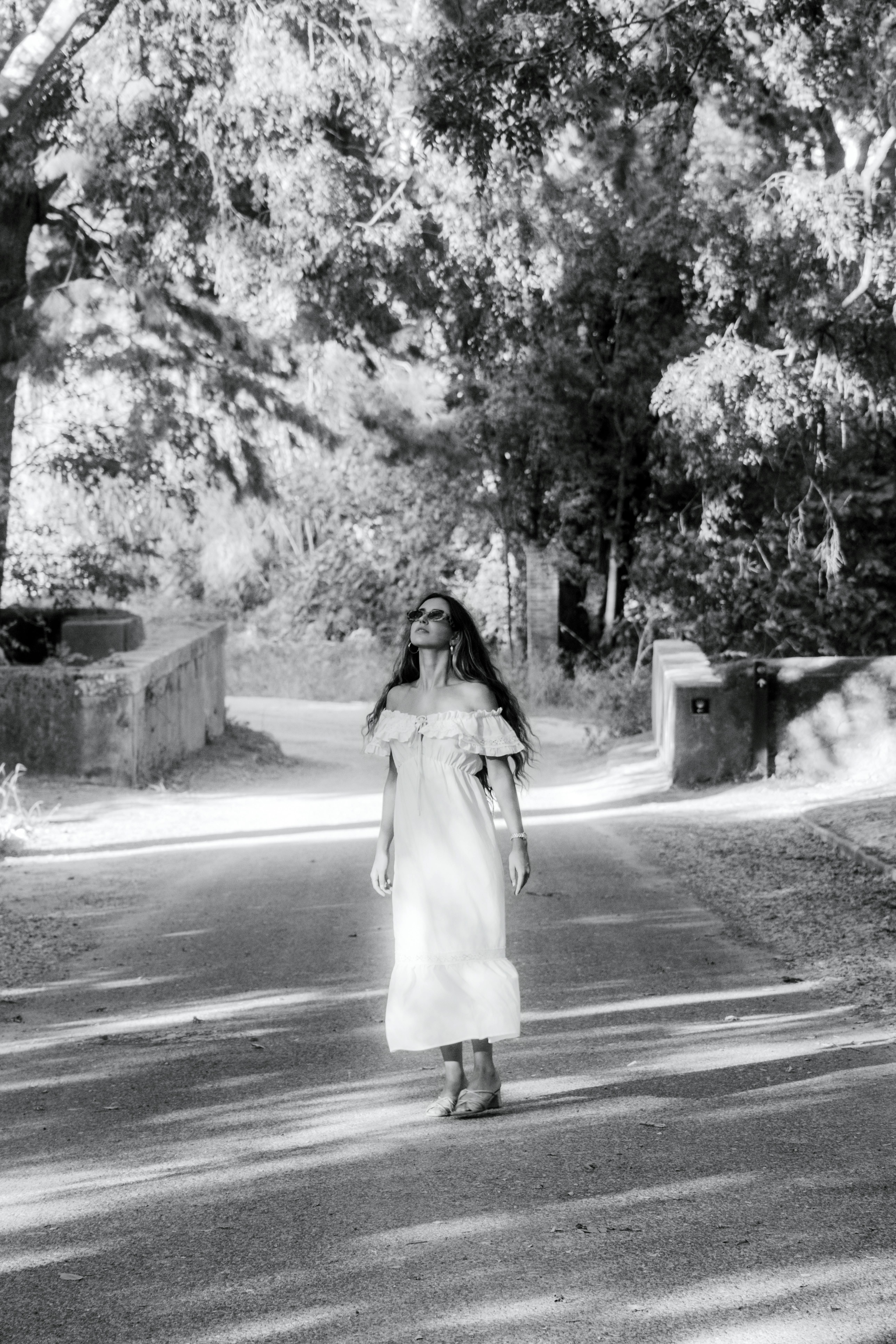 Black and white photo of a woman in a dress standing on a tree-lined path in Lisbon.