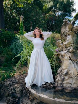 Portrait of a woman in a white dress standing by a fountain in Lisbon.