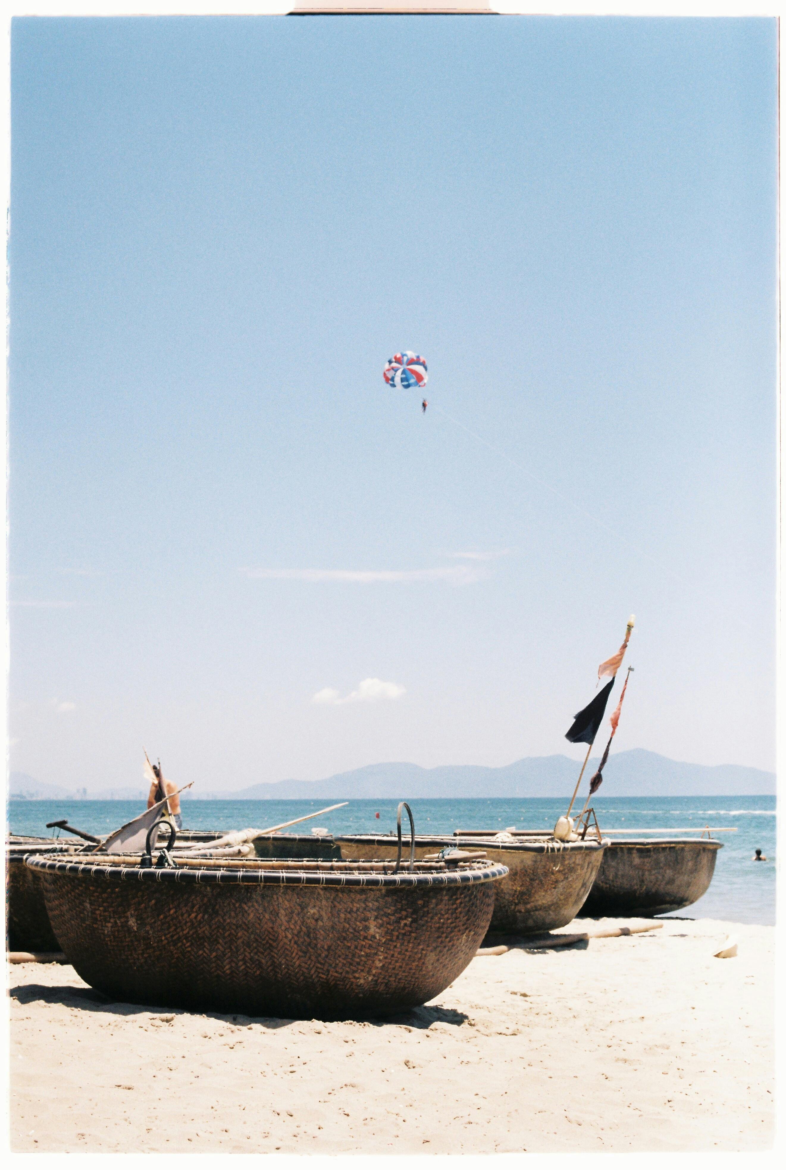 Traditional basket boats on Hội An beach with a parasail in the clear sky.