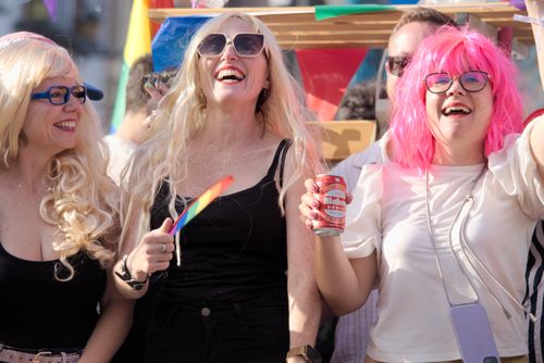 Free Three women joyfully celebrating at a vibrant festival with colorful decorations in Sevilla. Stock Photo