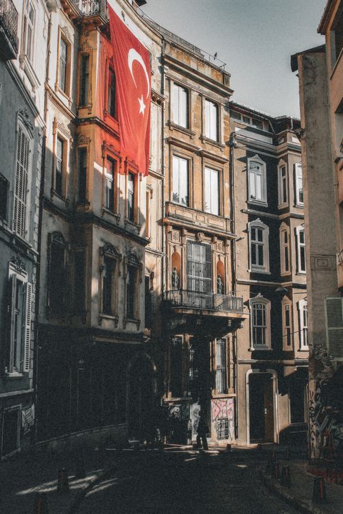 Free Turkish flag hanging from a historic building facade in an urban setting, showcasing architectural details. Stock Photo