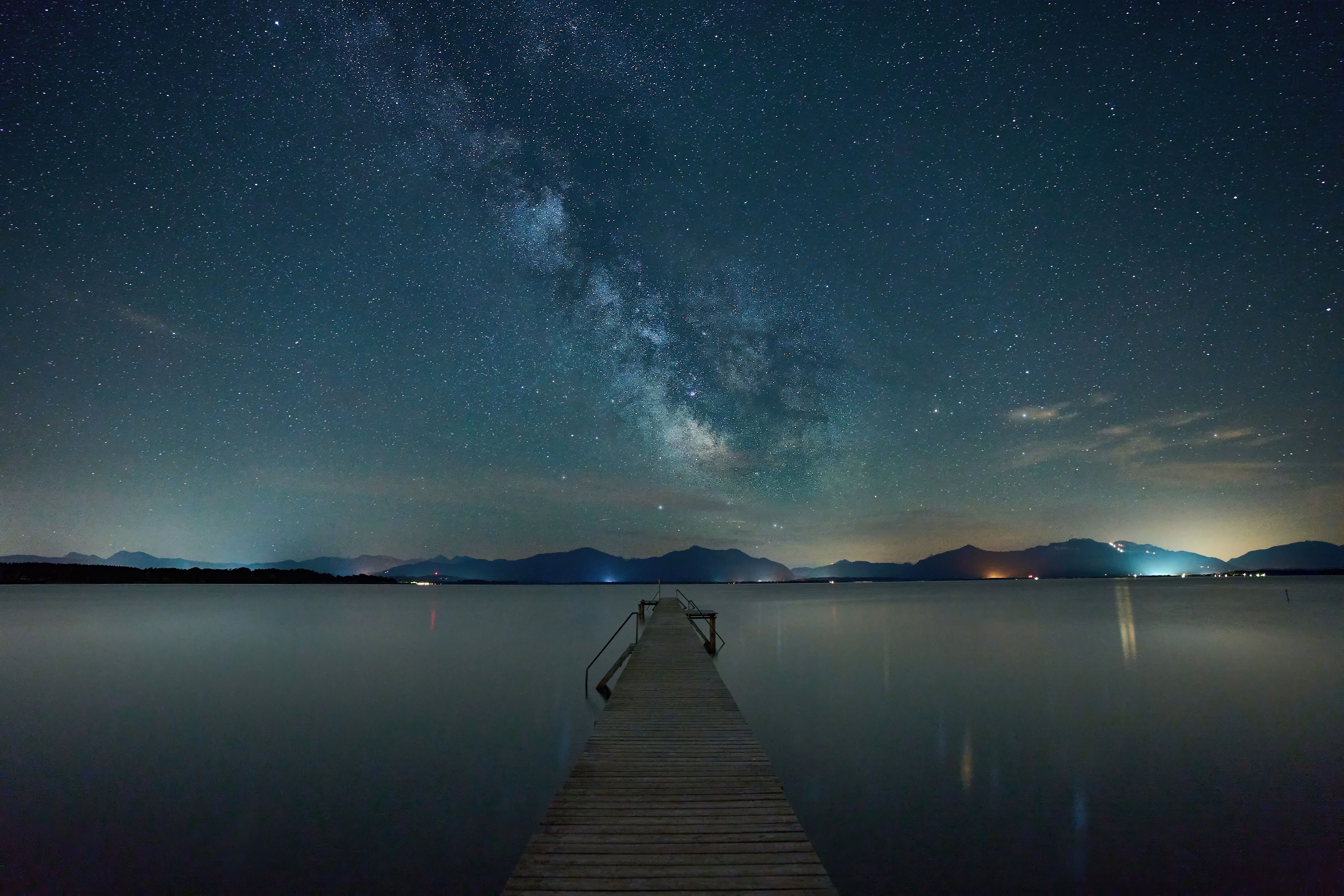 Captivating night sky with Milky Way over tranquil Seeon Lake pier.