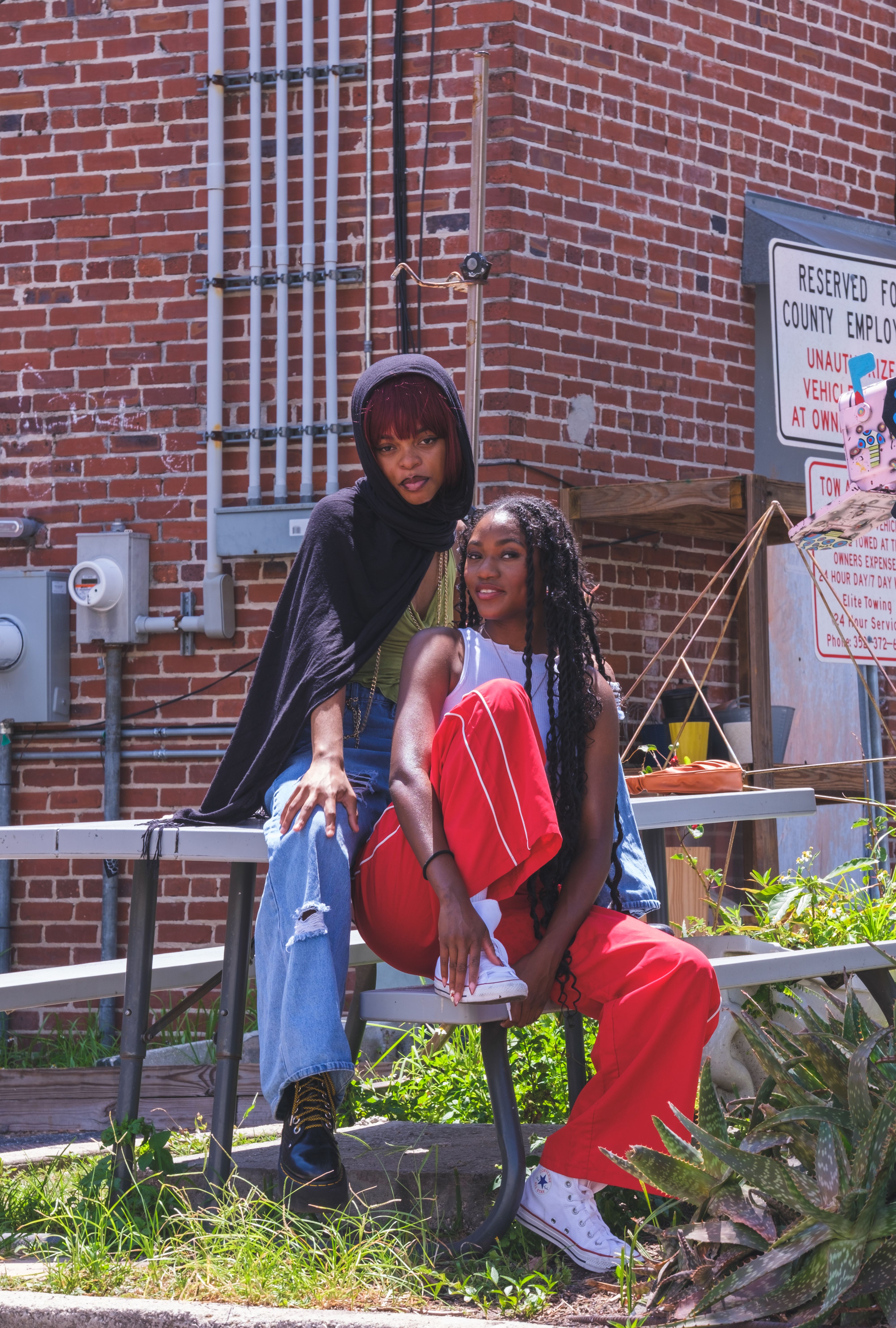 Two women showcasing colorful street fashion seated against a brick wall in Gainesville, FL.