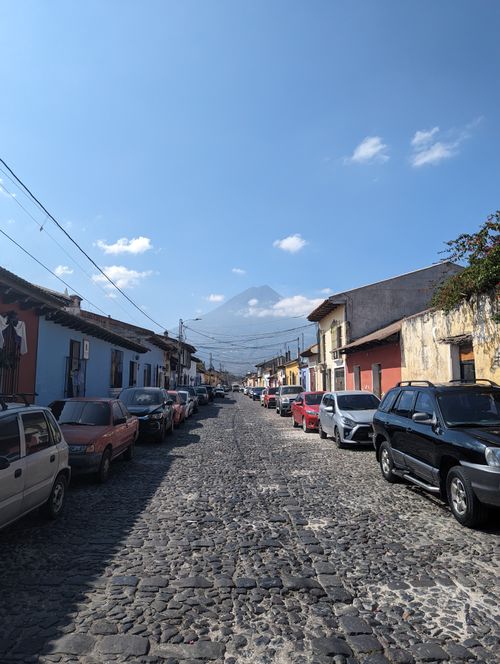 Free Historic cobblestone street in Antigua Guatemala with distant volcano view under clear blue skies. Stock Photo