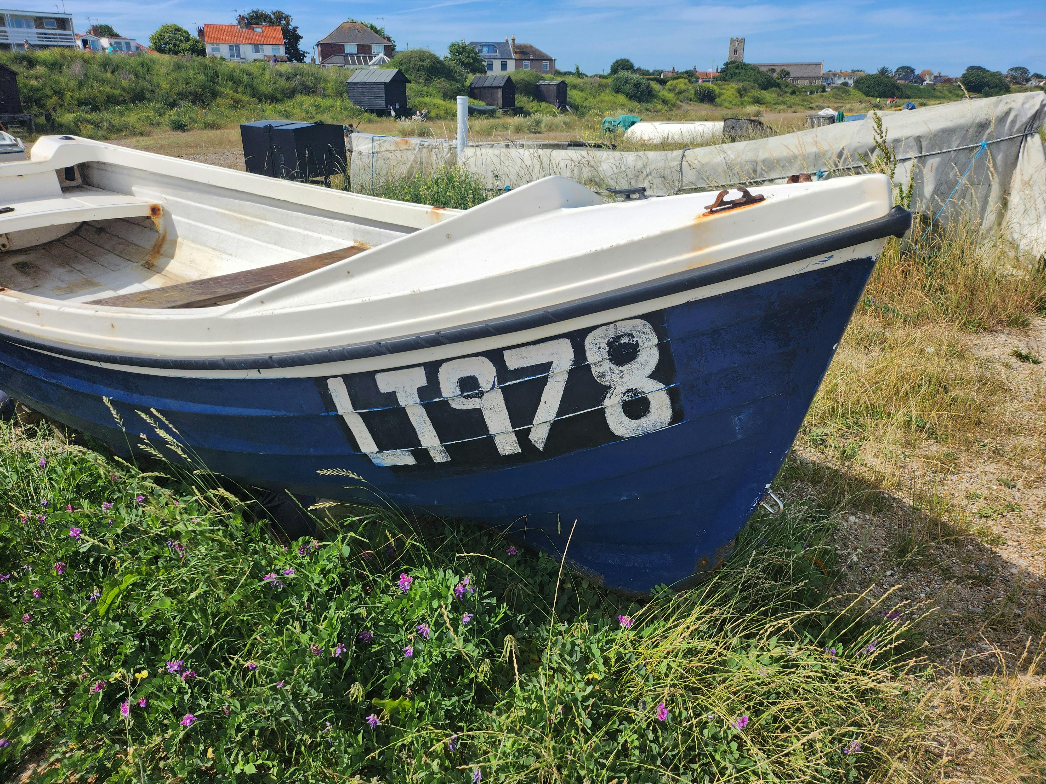 A weathered blue boat on a grassy landscape in a rural English village.