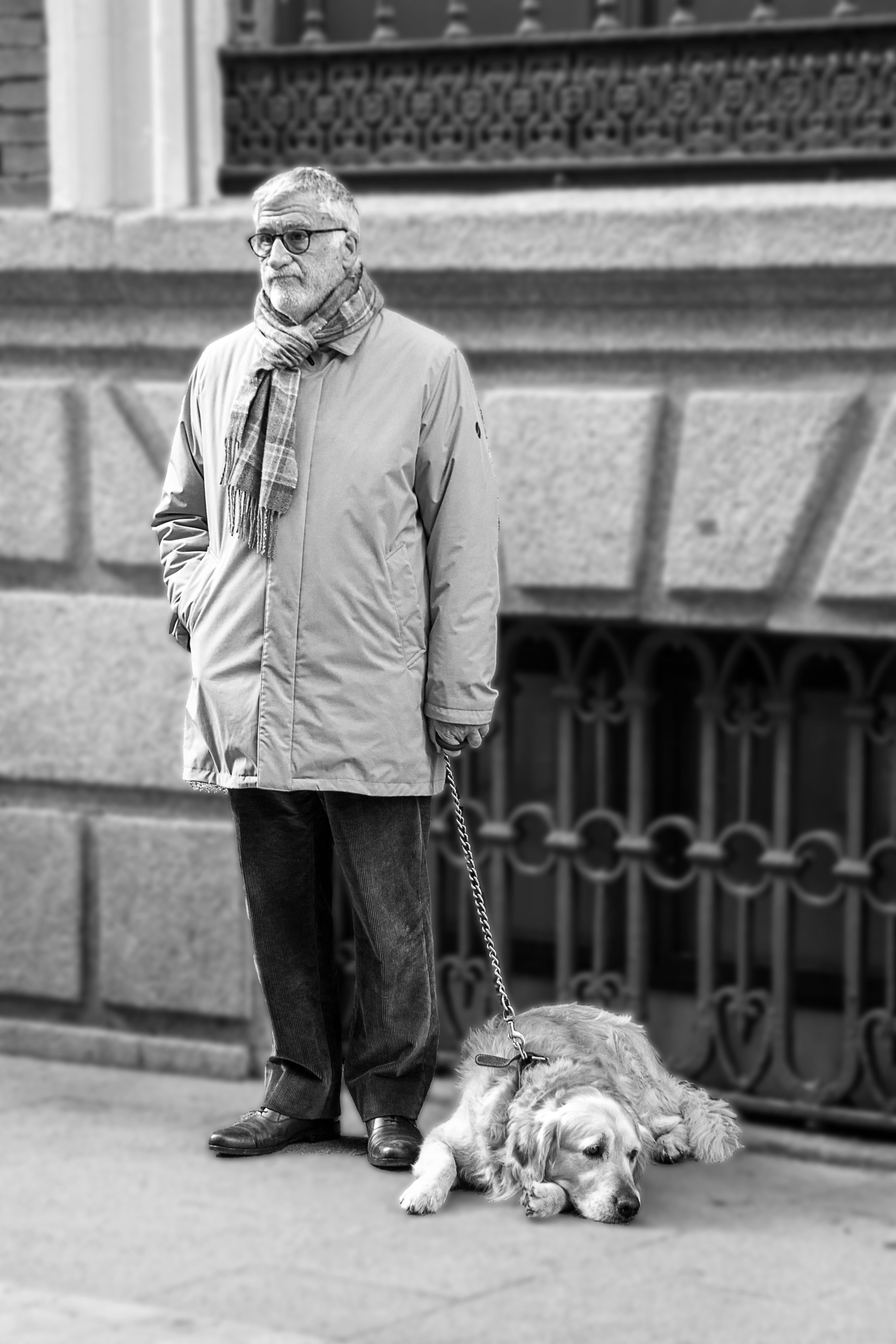 Black and white portrait of an elderly man standing with his dog in a city setting.