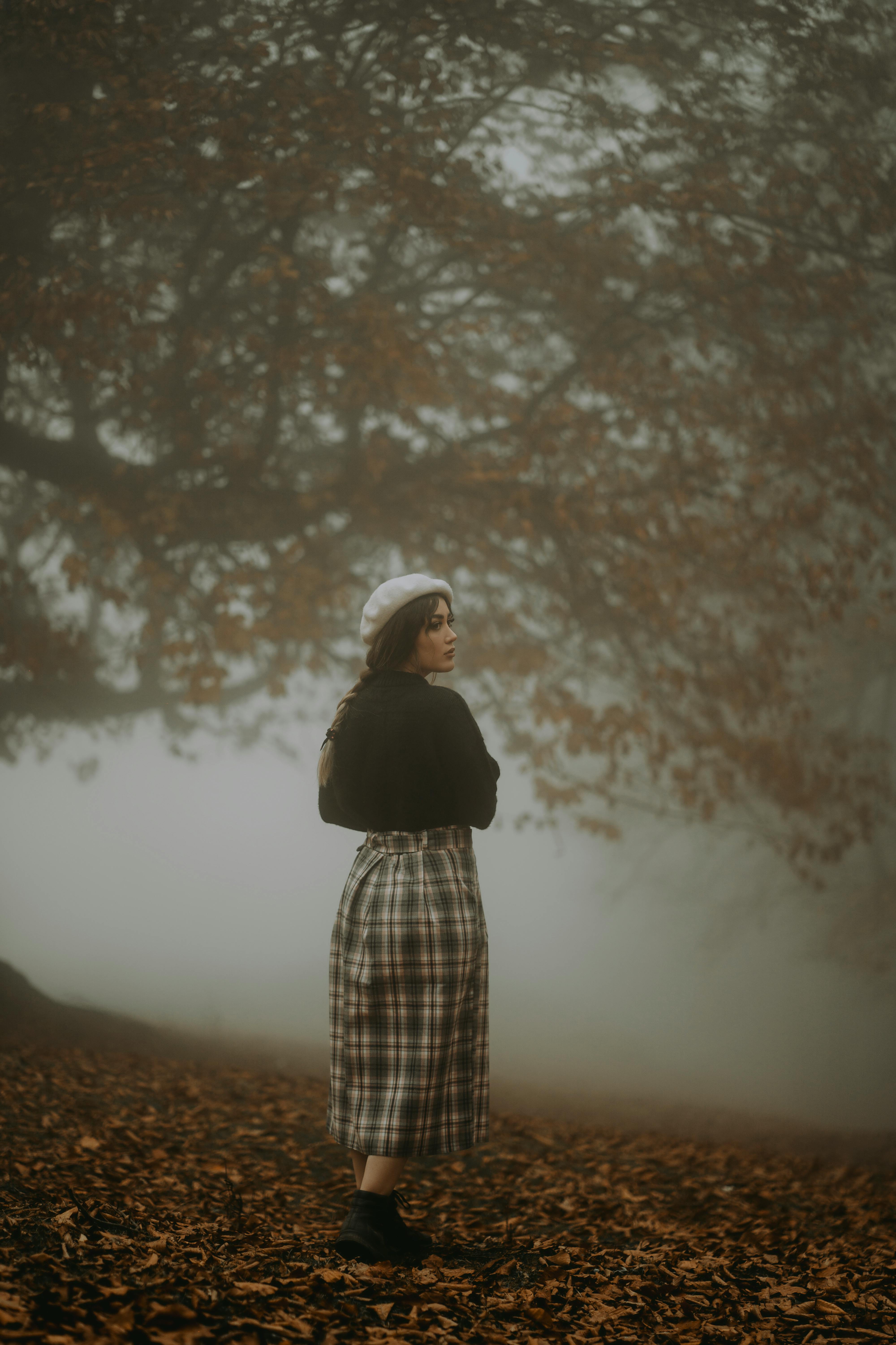 Stylish woman in beret stands in a foggy autumn forest, epitomizing seasonal fashion.