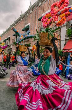 Mexican women in traditional dresses performing a lively street dance during a cultural festival.