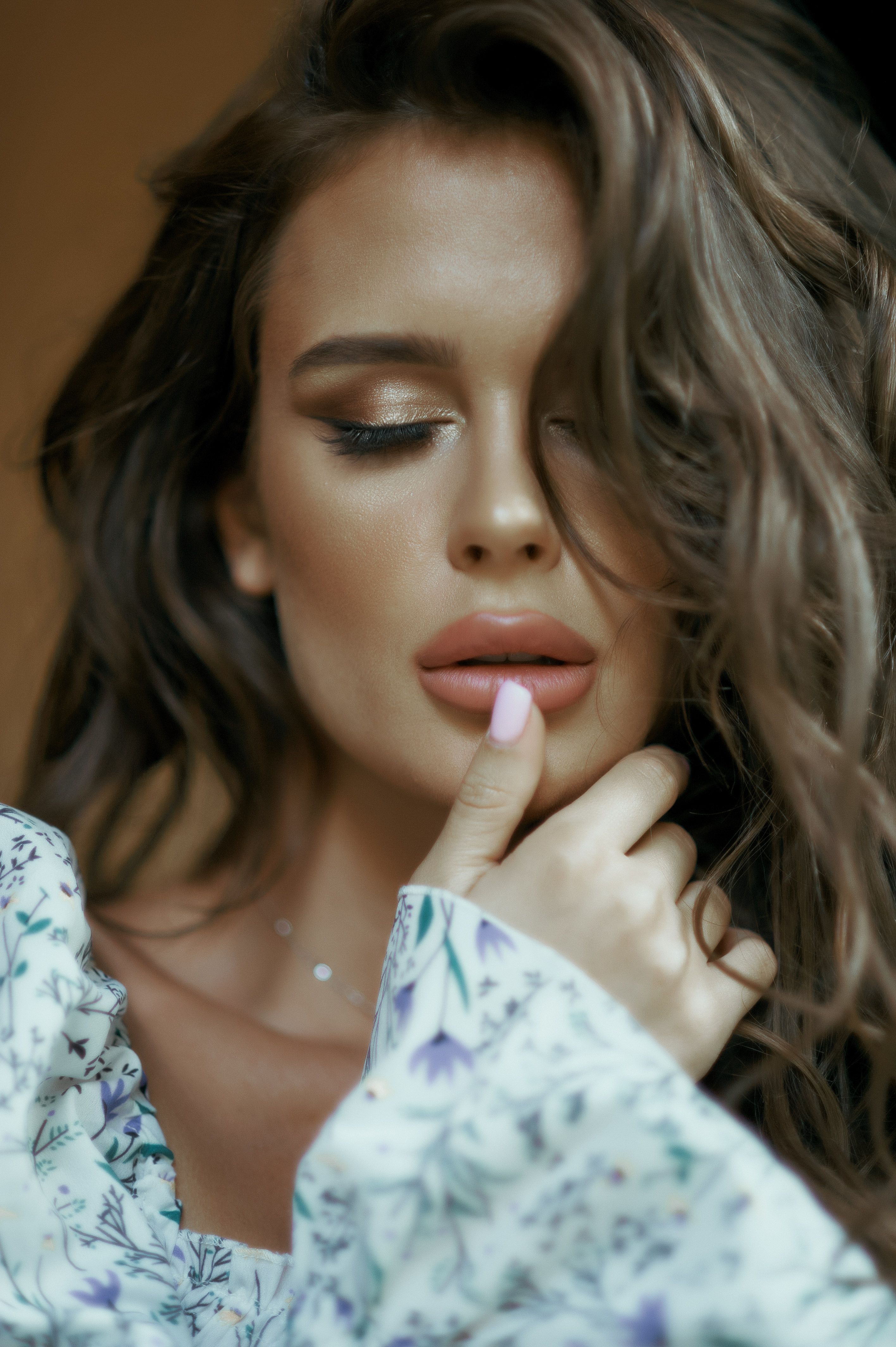 Close-up portrait of a woman with brown hair and eyes closed, wearing a floral blouse and displaying fashion elegance.