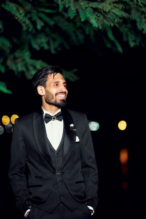 Free A smiling groom in a black suit standing outdoors at night, capturing elegance and style. Ideal for wedding themes. Stock Photo
