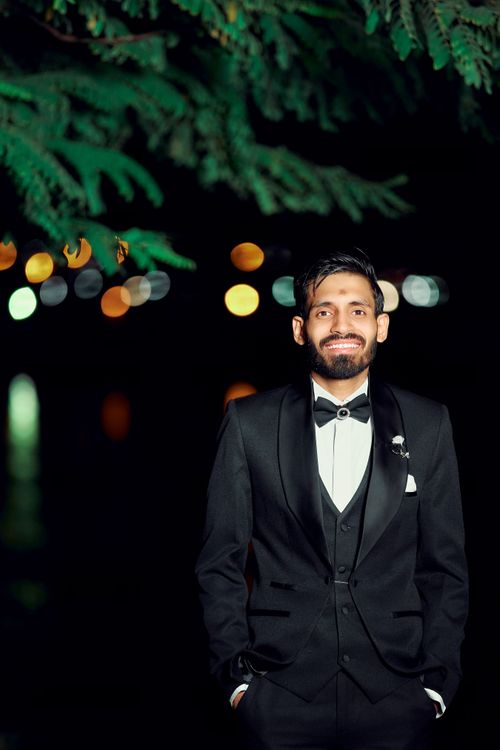 Free Portrait of a man in a black suit standing outside at night, illuminated by bokeh lights. Stock Photo