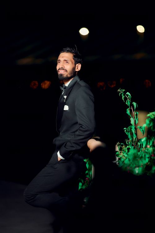 Free A well-dressed groom in a black suit poses confidently at a nighttime wedding celebration. Stock Photo