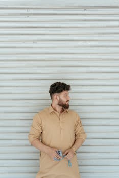 Man in traditional brown outfit standing with smartphone, looking away from camera.
