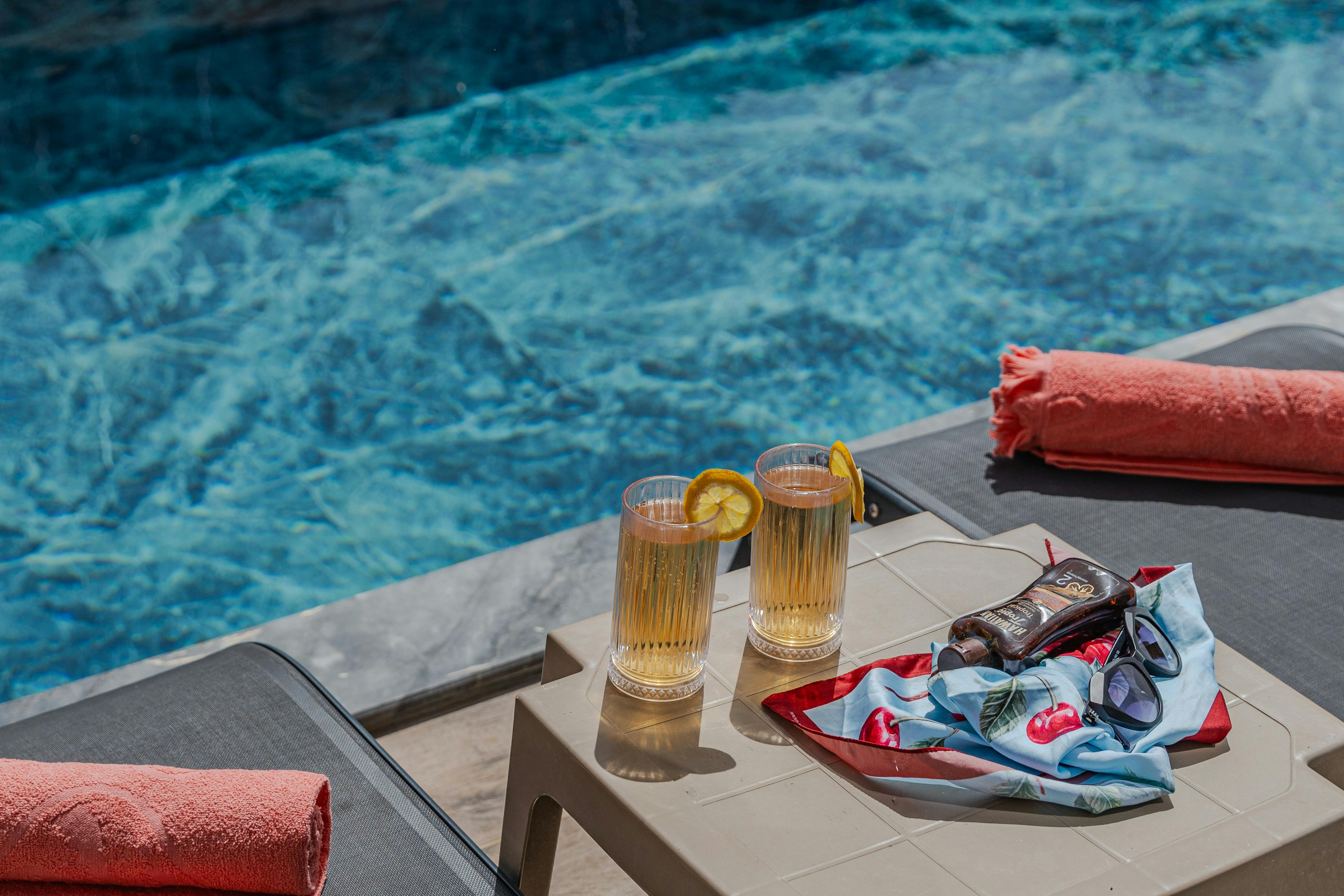 a table with two glasses and a towel next to a pool