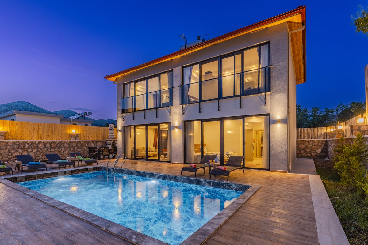 A white two-storey house with a lit pool at twilight
