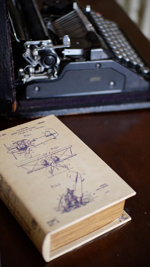 Free A classic typewriter beside a book filled with vintage engineering schematics, creating a nostalgic ambiance. Stock Photo