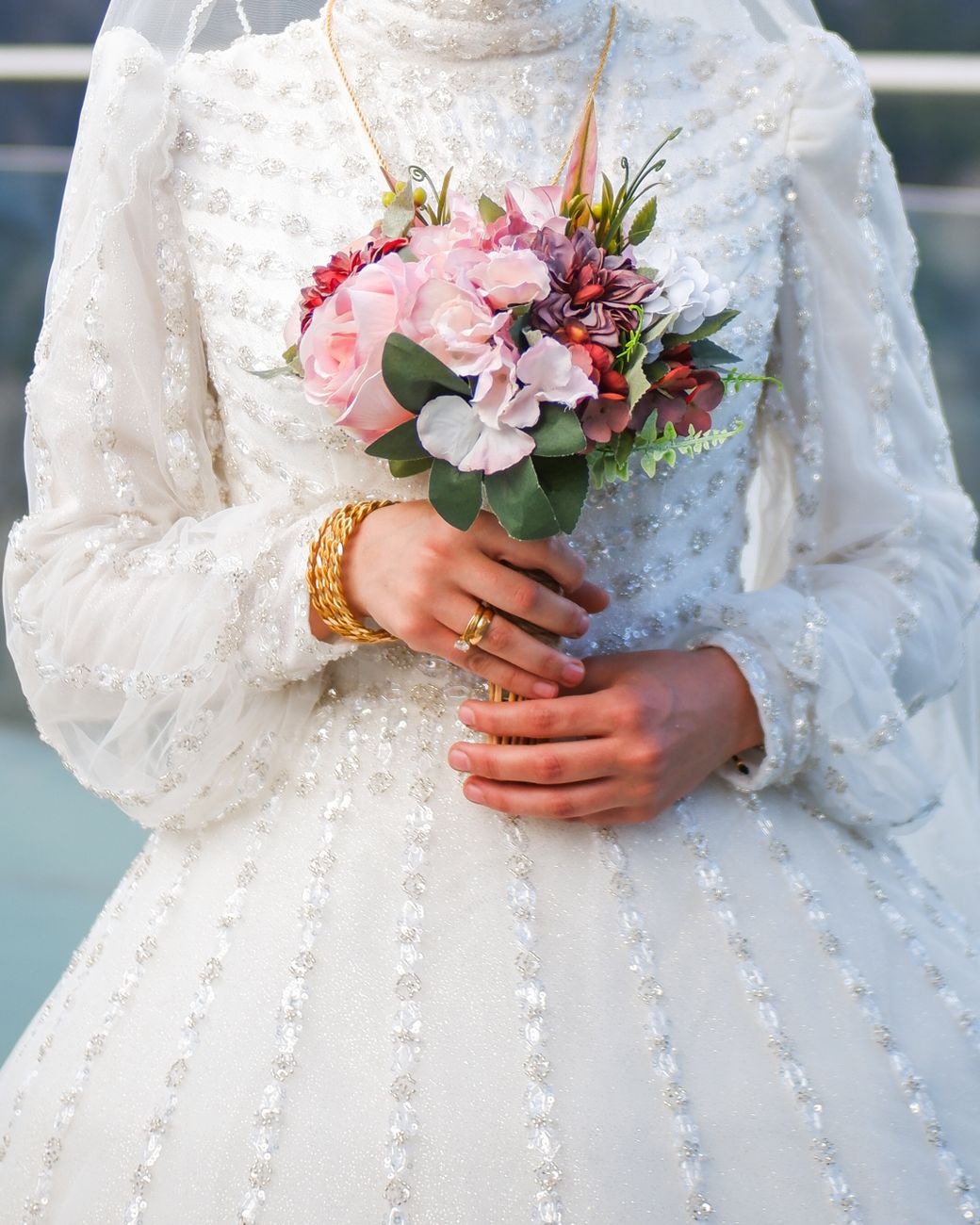 Close-up of a bride holding a colorful bouquet wearing a detailed wedding dress.