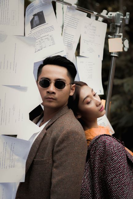 Asian man and woman posing back to back in a creative outdoor setting with documents.