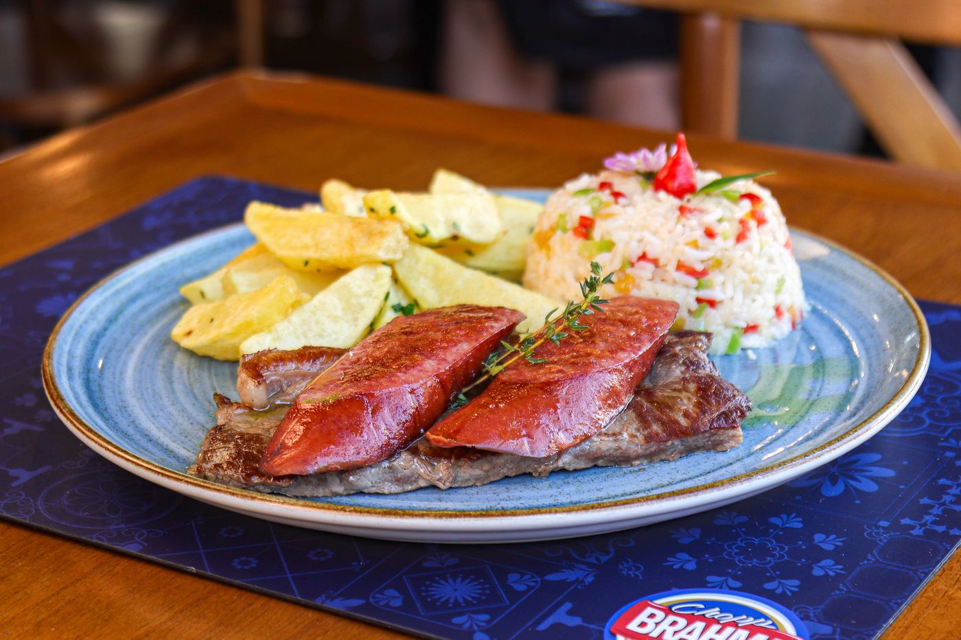 Close-up of a steak served with rice and potatoes on a decorated plate.
