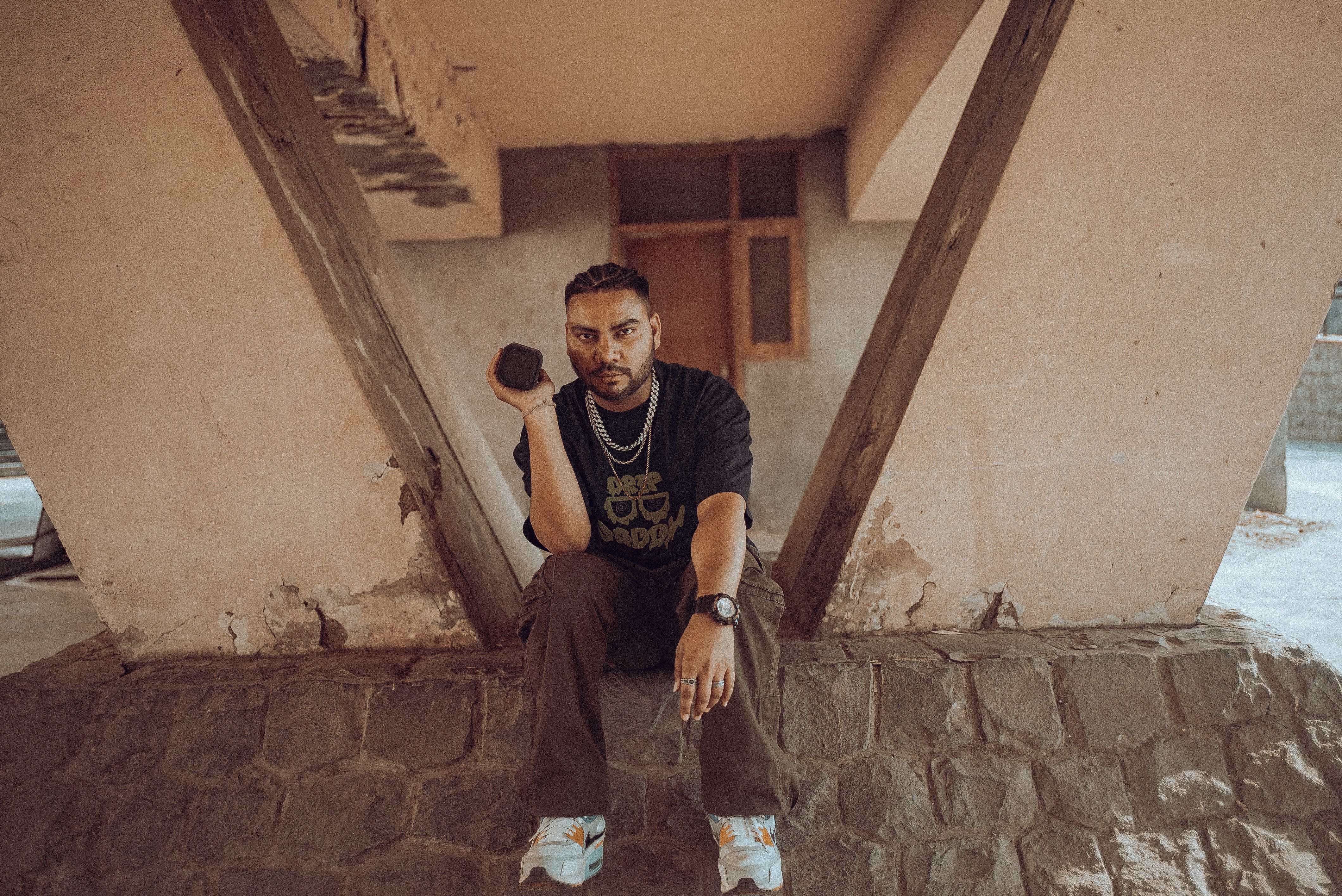 Stylish portrait of a man sitting under a unique structure in New Delhi, showcasing urban fashion.