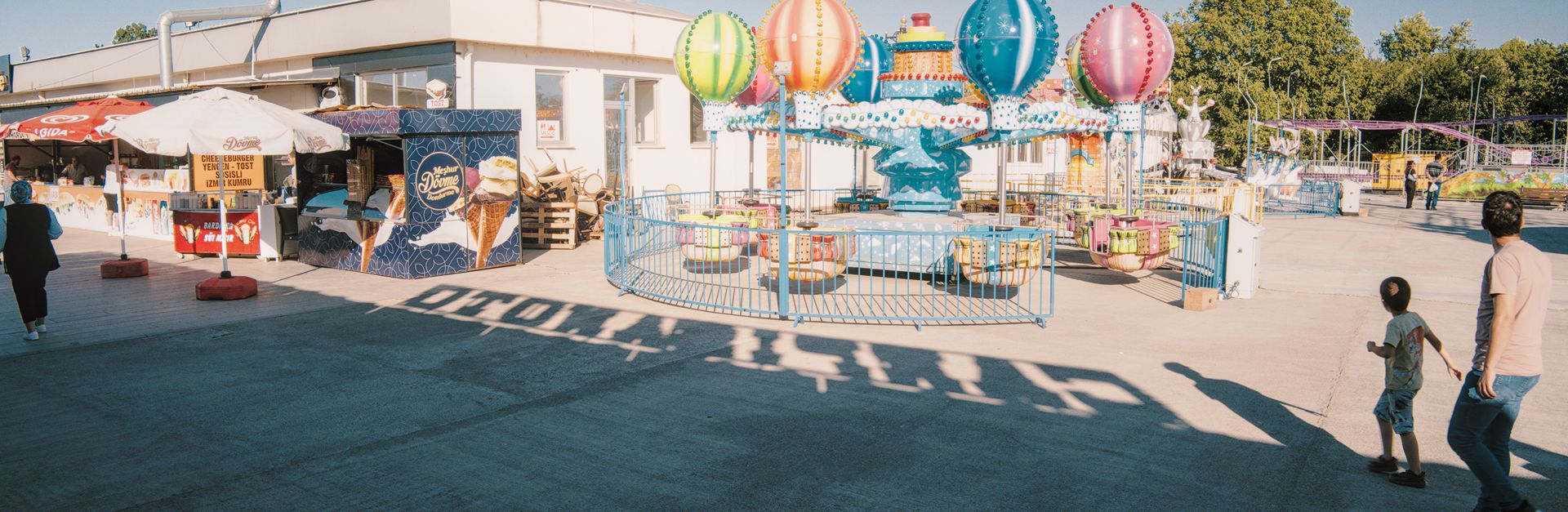 Colorful carnival scene with balloon ride and visitors enjoying a sunny day outdoors.