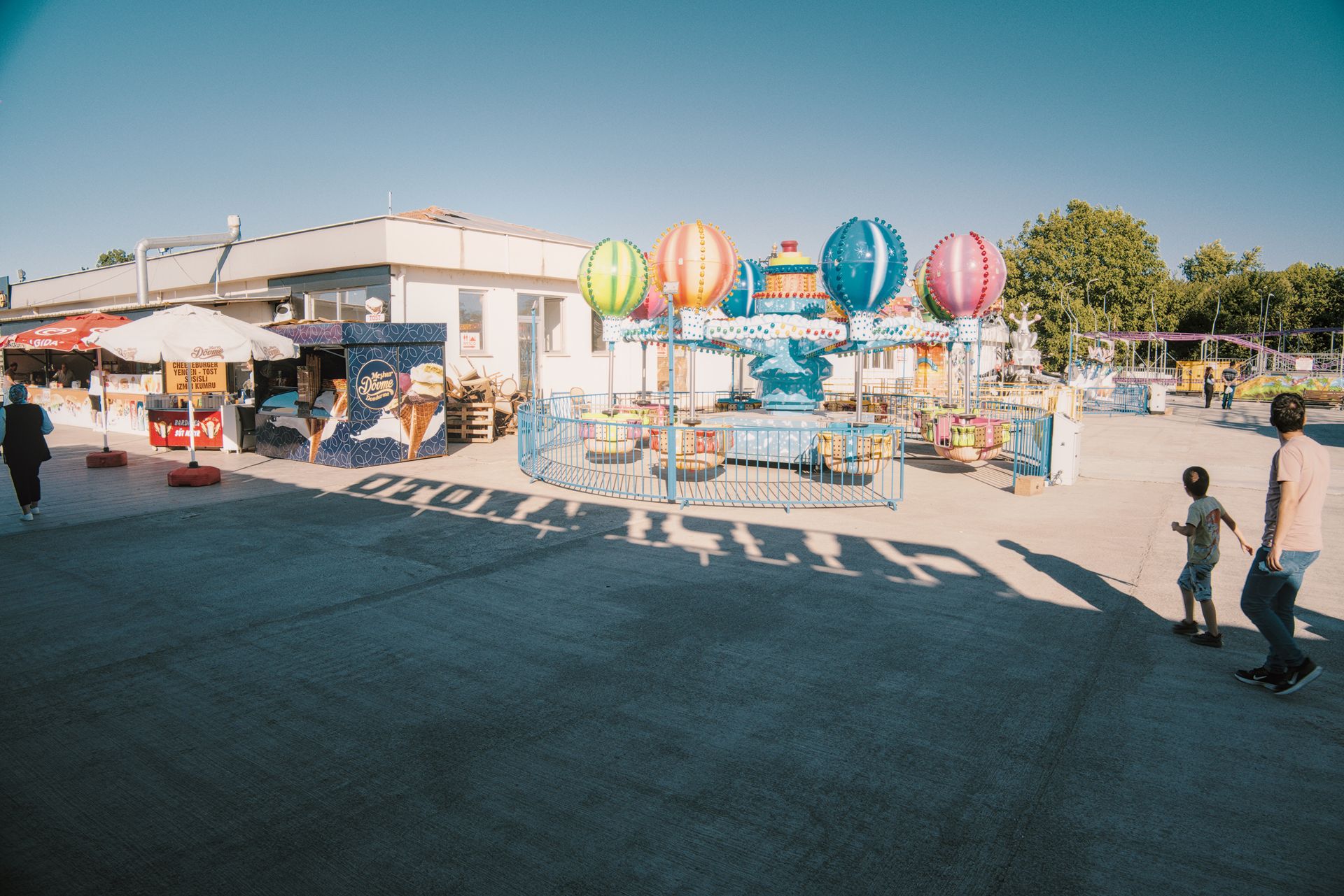 Colorful carnival scene with balloon ride and visitors enjoying a sunny day outdoors.