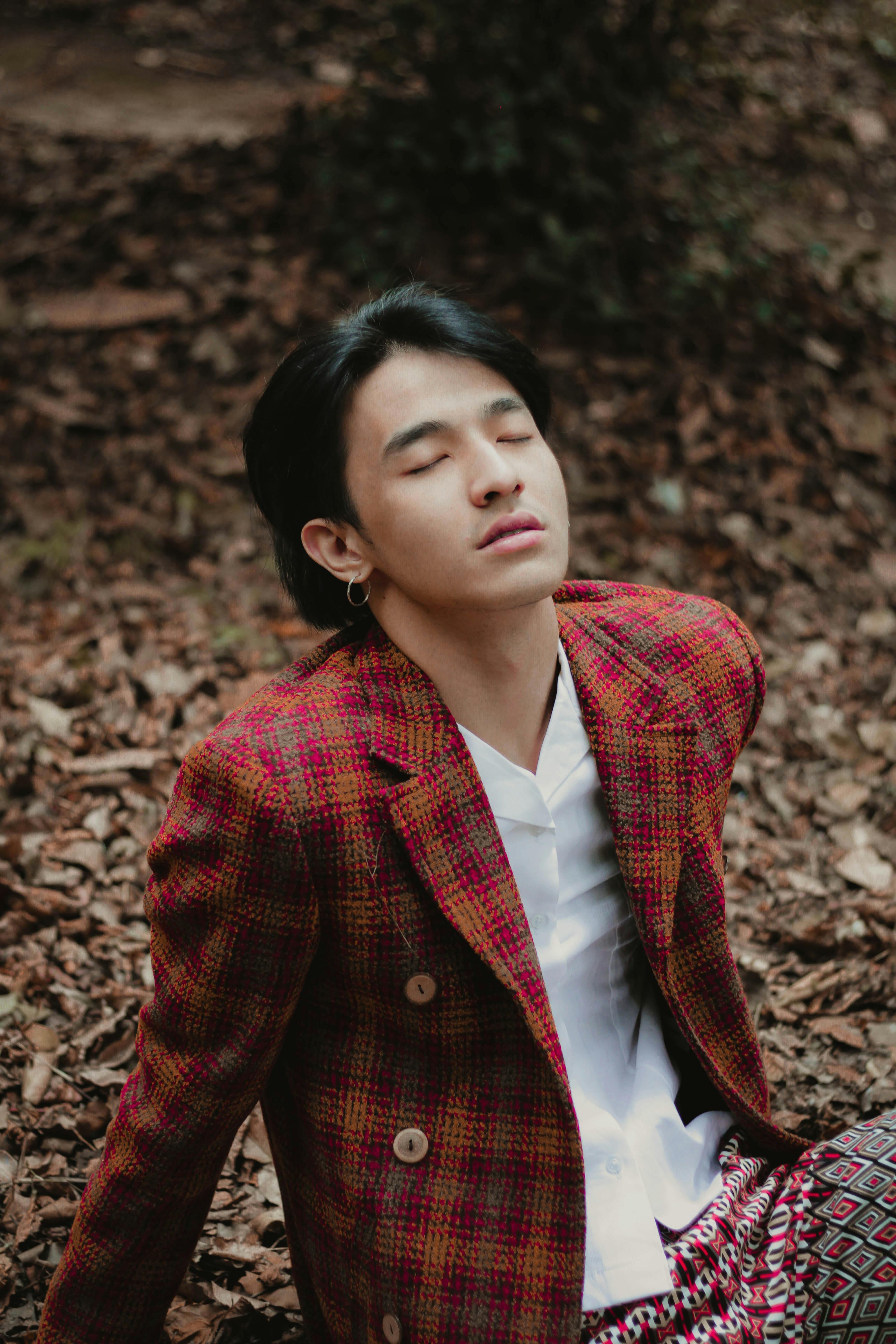Young man relaxing in a stylish jacket, surrounded by fallen leaves, outdoors.