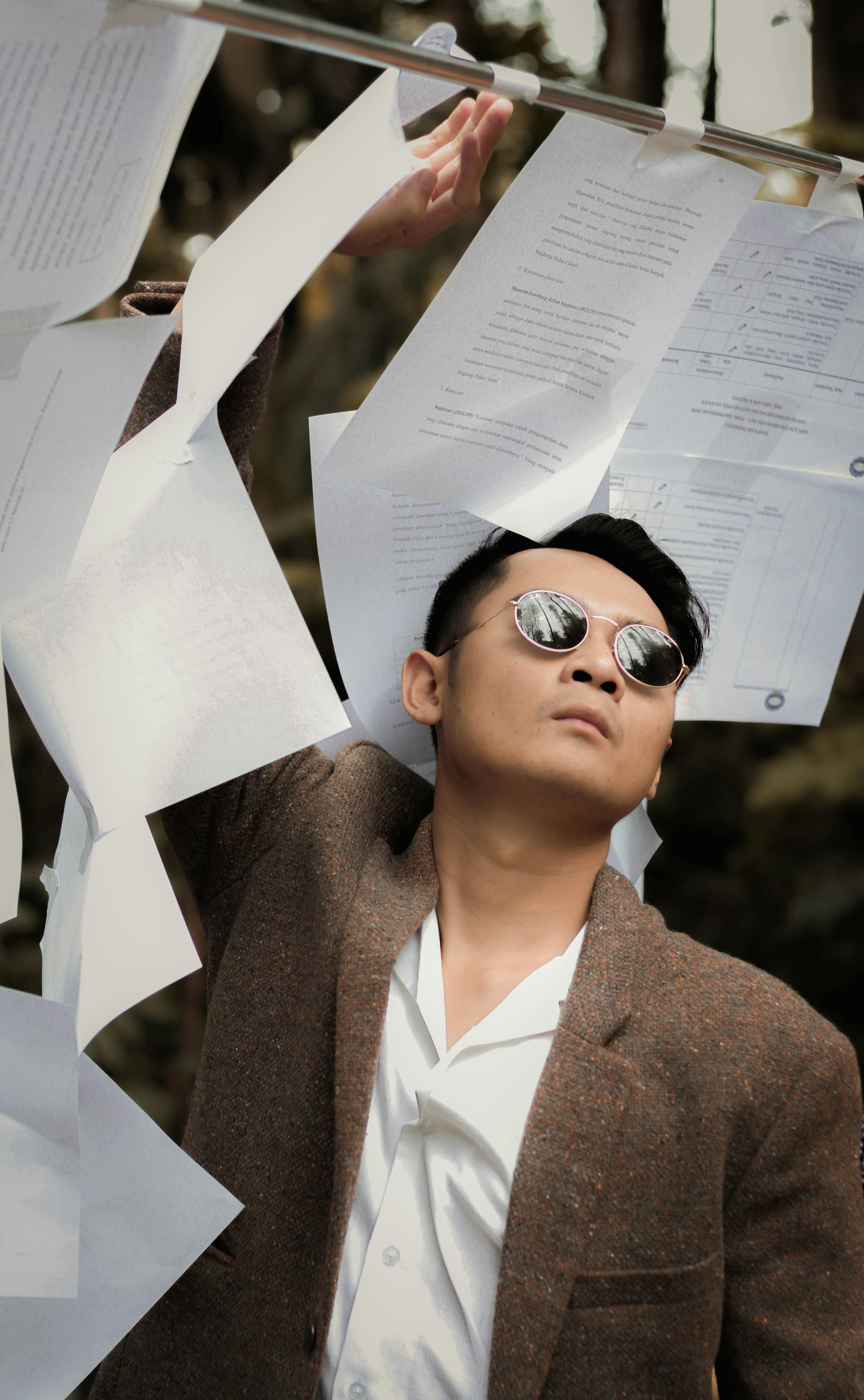 一位戴着墨镜的时尚男士在户外与飞舞的纸张合影，尽显风格与自信