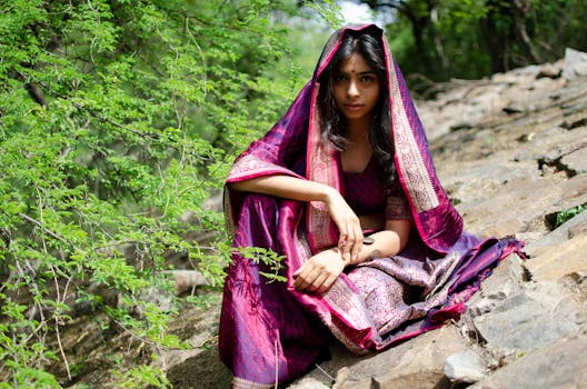 A beautiful South Asian woman in a traditional saree poses outdoors on a rocky path.