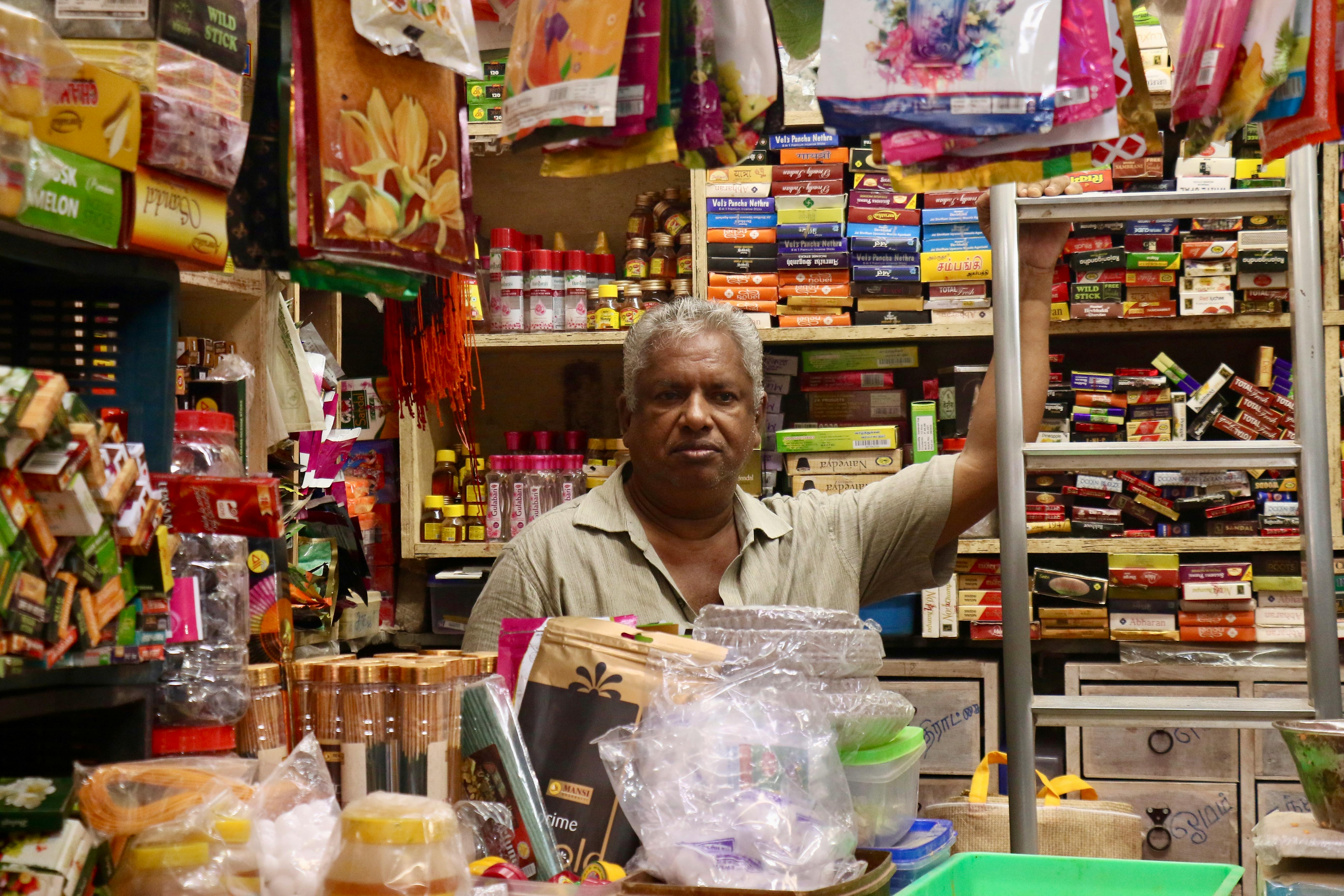 A middle-aged man working in a colorful, bustling Indian grocery store filled with diverse products.