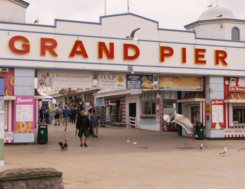 Entrance of the Grand Pier with people and seagulls, featuring shops and vibrant signage.