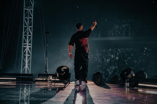 An energetic rapper performing on stage in Tirana, with a vibrant crowd and powerful stage lights.