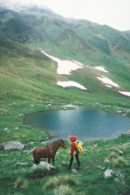 Serene mountain landscape featuring a lone hiker and horse by a tranquil lake in Georgia.