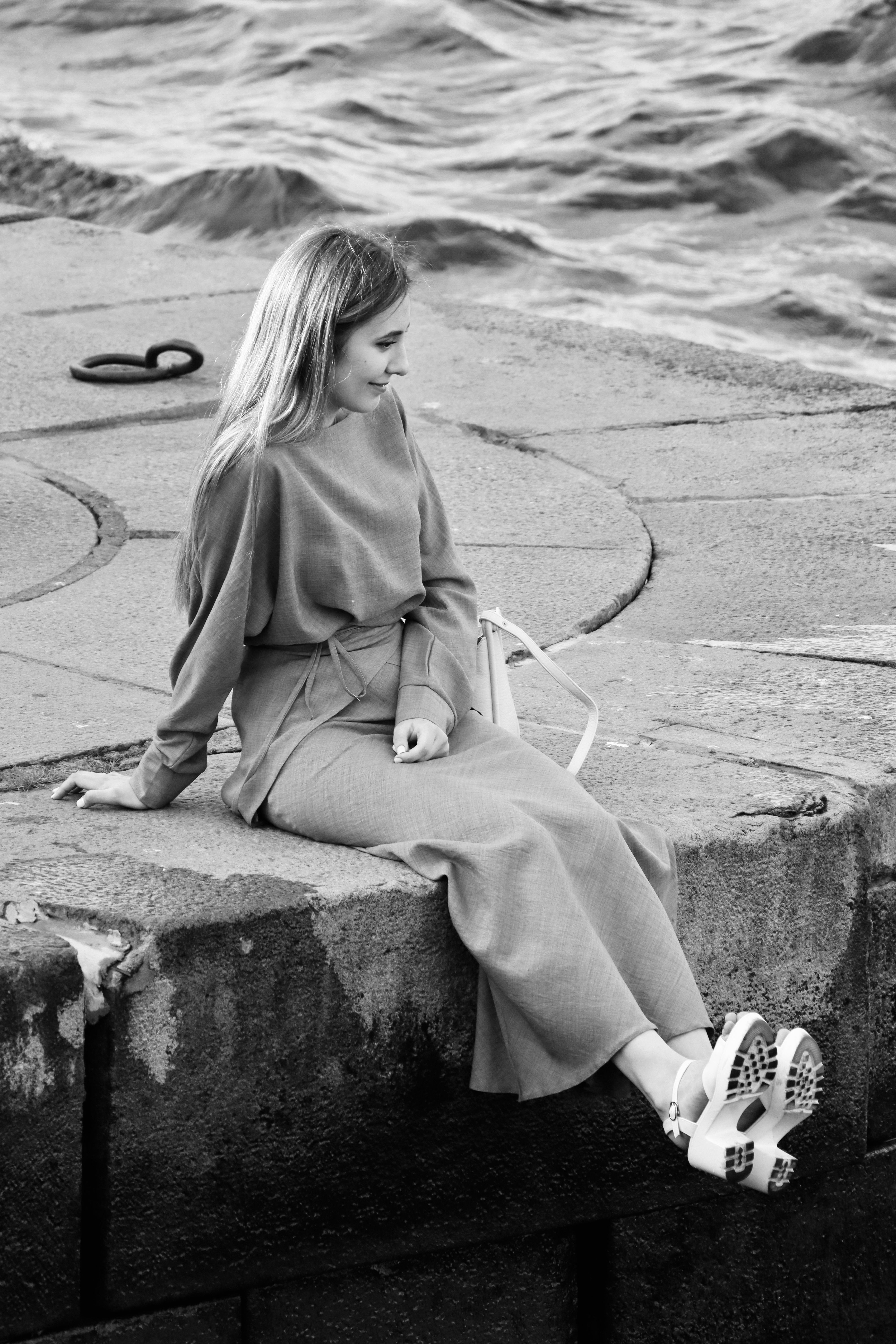 A woman sitting on a concrete wall near the water · Free Stock Photo