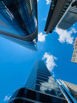A dramatic upward view of modern skyscrapers against a clear blue sky and clouds.