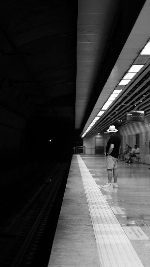 Free Black and white photo of a man in a hat waiting at an underground station platform at night. Stock Photo