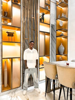 A smiling man poses in a chic, modern interior with illuminated shelves.