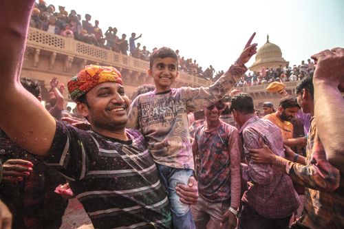 Free A father and son celebrating the vibrant Holi festival in India, surrounded by a cheerful crowd. Stock Photo