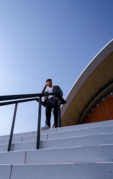 Businessman ascending stairs beside modern Berlin architecture under clear blue sky.