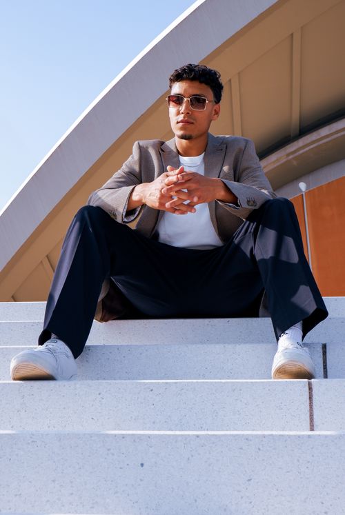 Free Confident man in sunglasses and blazer sitting on steps with Berlin architecture background. Stock Photo