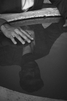 A man's reflection on water creates a moody black and white composition.