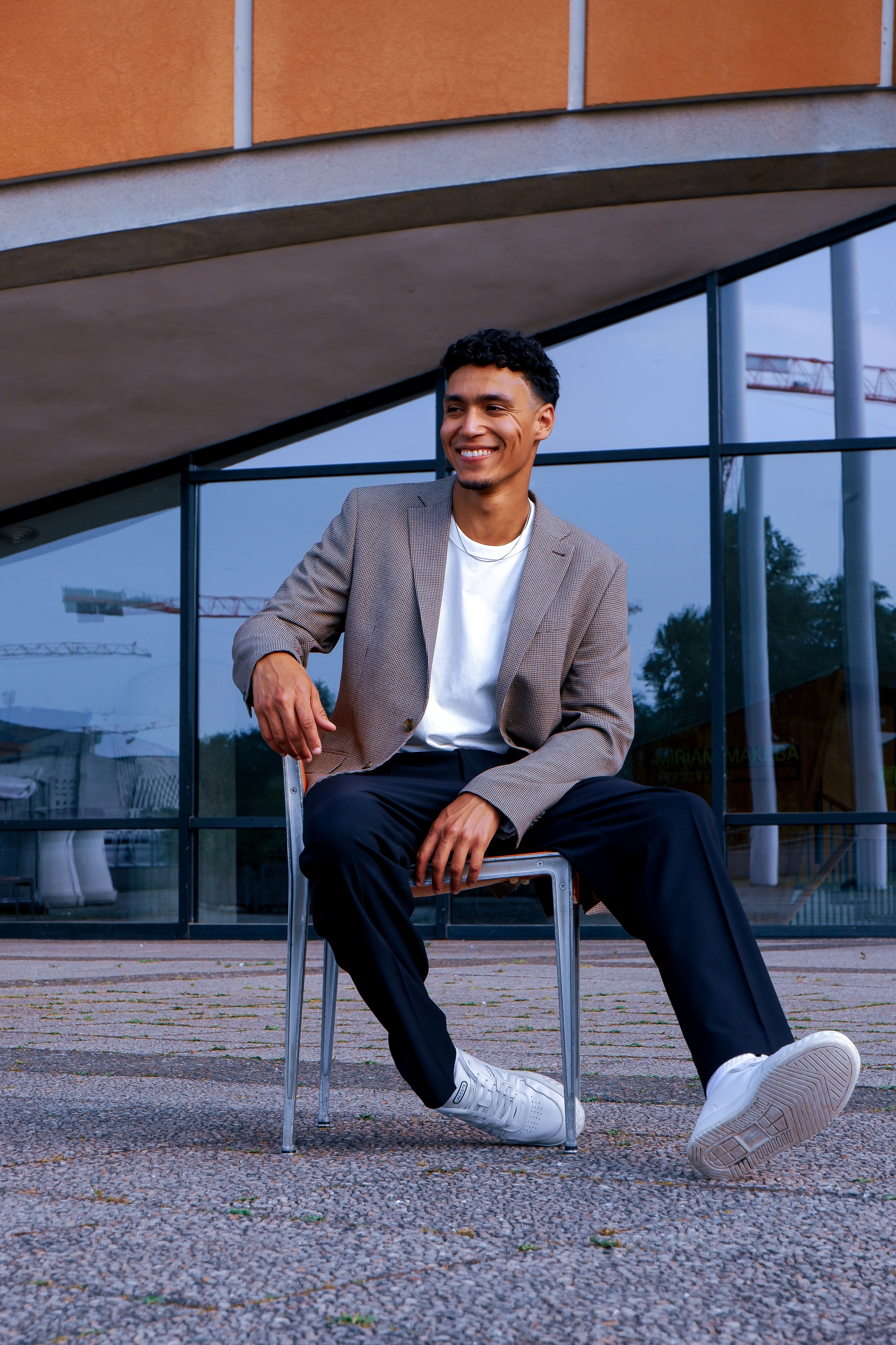 Fashionable man in urban setting, sitting and smiling outdoors in Berlin. Perfect for lifestyle or fashion themes.