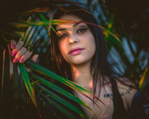 Free Captivating portrait of a woman with striking features surrounded by lush green foliage. A mix of natural and stylish. Stock Photo