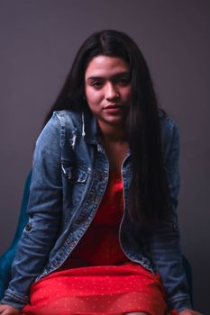 Stylish woman in a denim jacket sitting indoors posing elegantly.