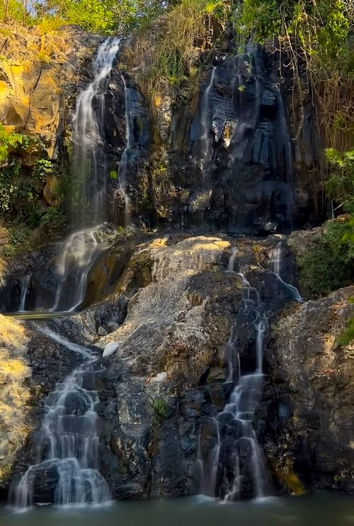 Free Scenic waterfall cascading over rocks surrounded by lush greenery in daylight. Stock Photo