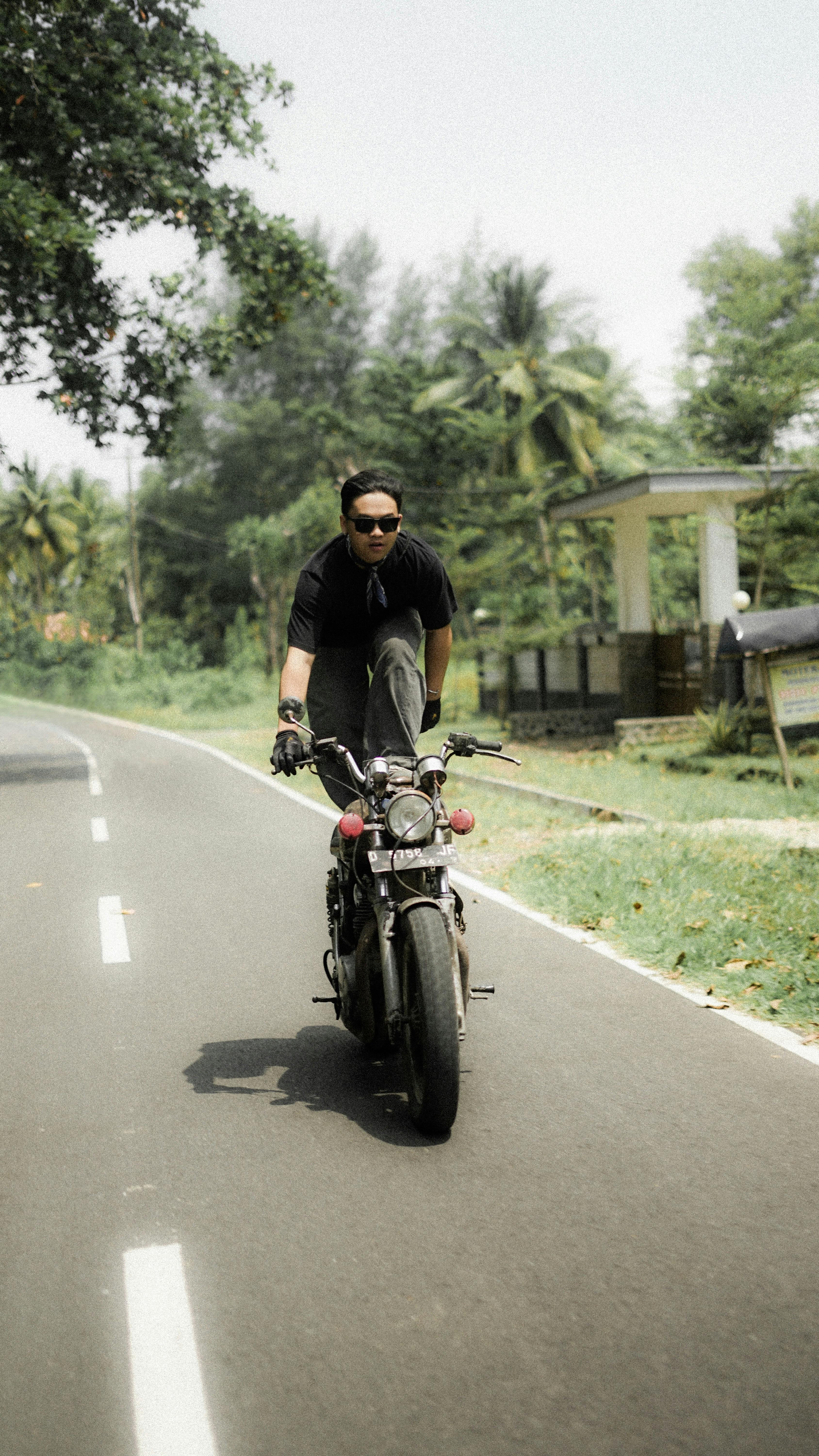 Young man doing a motorcycle stunt on a rural road, showcasing bravery and adventure.