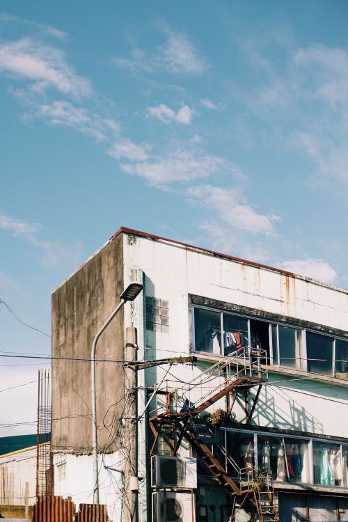 Free A decaying urban building with exposed wires and external staircase under a clear sky. Stock Photo
