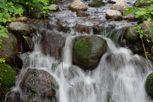 Free A picturesque waterfall flowing over moss-covered rocks in a lush forest landscape. Stock Photo