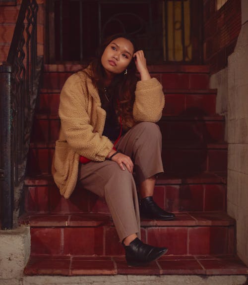 A Woman in Brown Coat Sitting on Stairs
